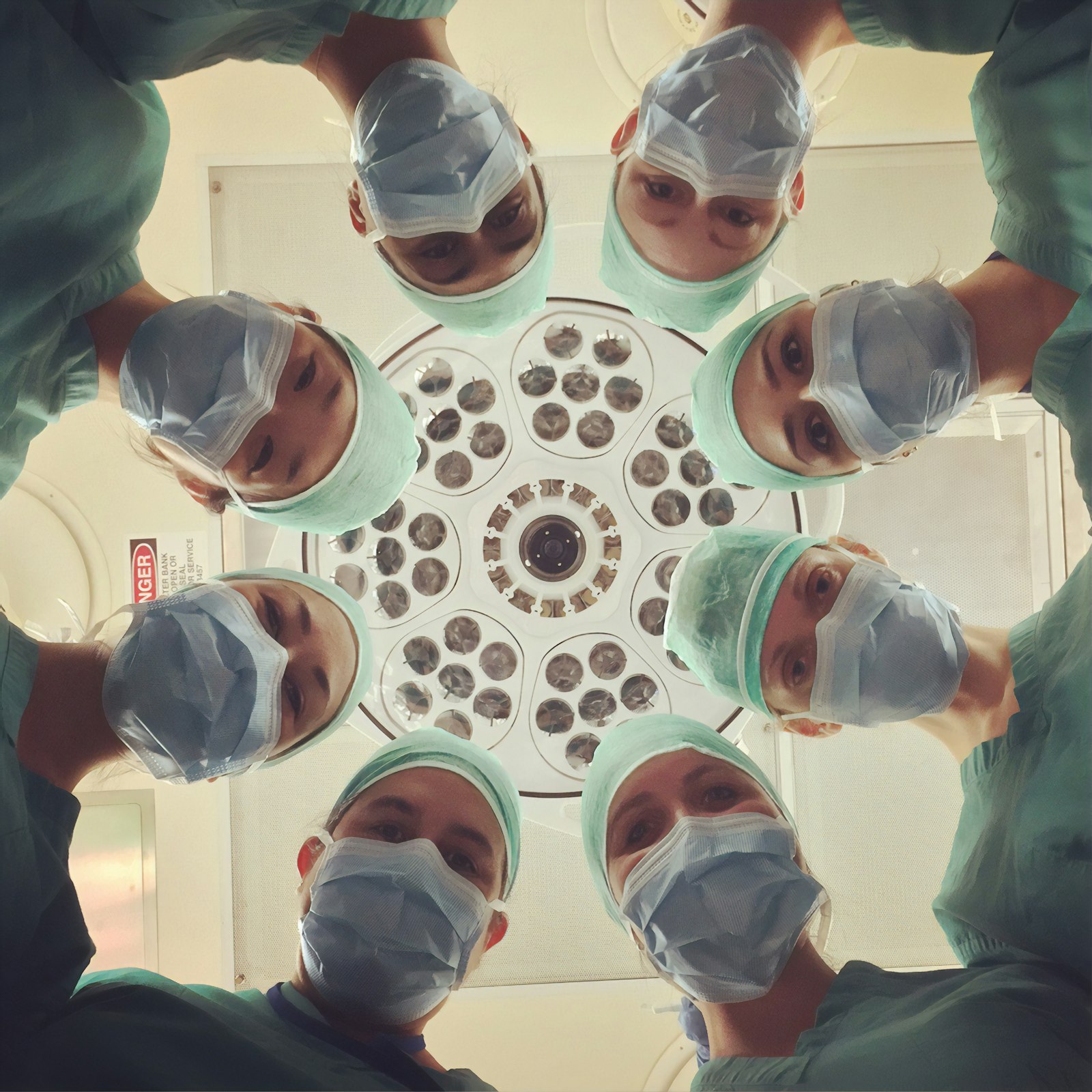 Clinical team in teal scrubs gathered under a surgical light, looking down as a group