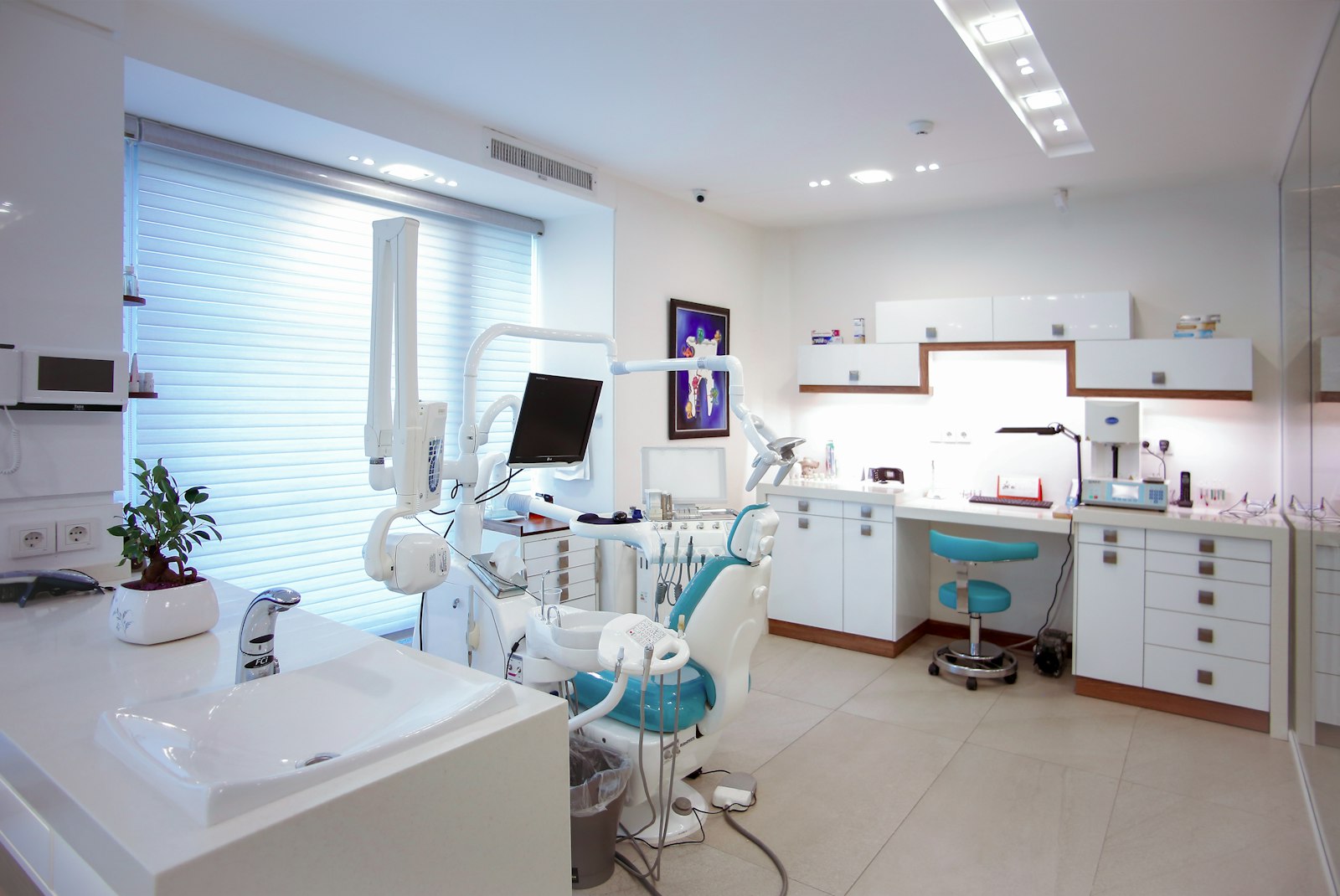 Modern clinic treatment room with a staff workstation and teal chairs